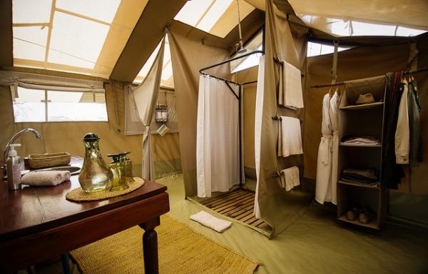 En-suite safari bathroom inside a tent featuring a classic bucket shower and vanity.