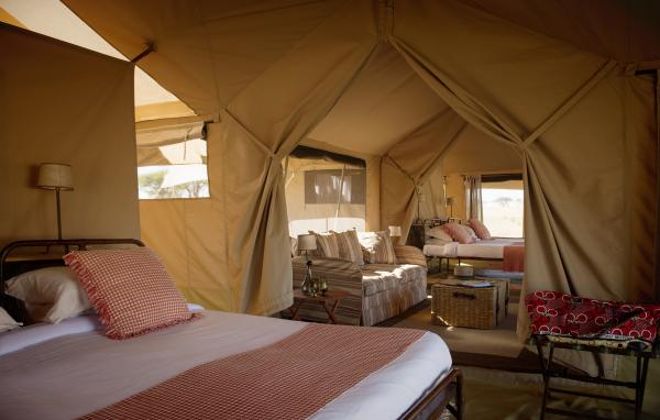 Interior of a luxury mobile safari tent featuring a large bed and high-quality linens.