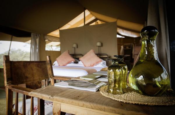 Detail of a rustic wooden writing desk inside a safari tent with views of the wild.